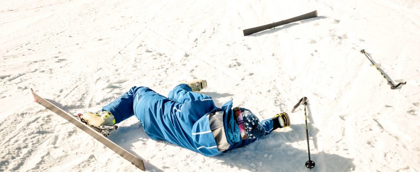 Professional skier after crash accident on skiing resort slope - Winter sport emergency concept with athlete needing help assistance on dramatic trouble situation - Warm sunny afternoon color tones