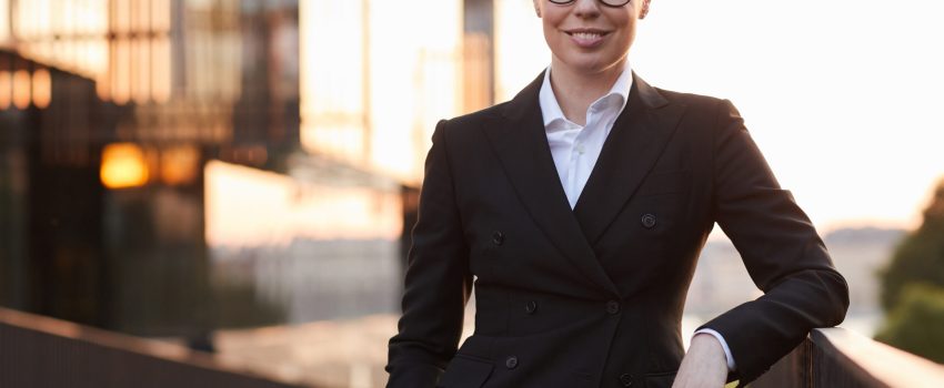 Portrait of mature businesswoman in eyeglasses and in black suit smiling at camera standing outdoors